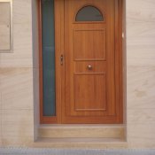 Puerta entrada lacada imitación madera con cerradura de seguridad y panel decorativo.